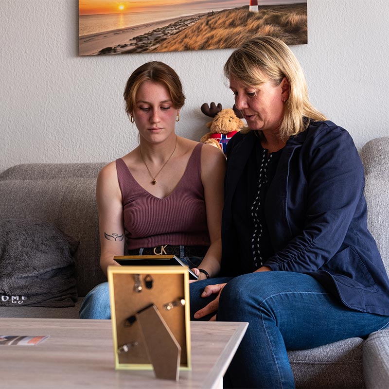 Mutter und Tochter sprechen auf dem Sofa sitzend liebevoll über einen Verstorbenen